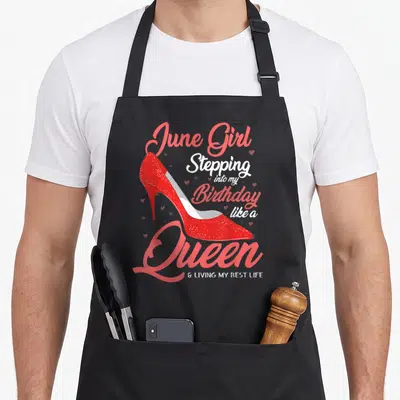 Stepping queen birthday apron - Red high heel shoe with June Girl Stepping into my Birthday like a Queen text — shown on a black cotton canvas apron against a white background