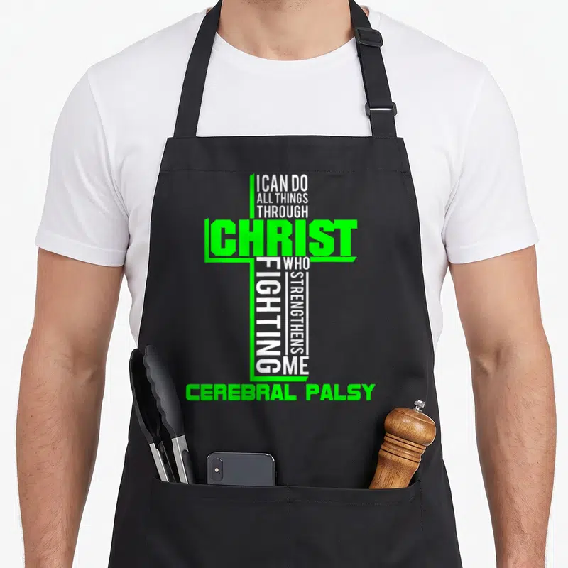 Through cerebral palsy awareness apron - Cross shape formed by white and green text reading I Can Do All Things Through — shown on a black cotton canvas apron against a white background