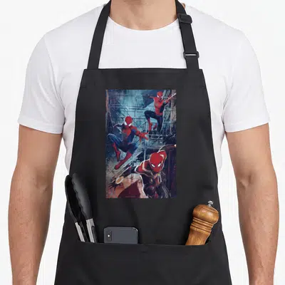 Way jump apron - Three Spider-Man figures in red and blue suits jumping against grey industrial scaffolding background — shown on a black cotton canvas apron against a white background