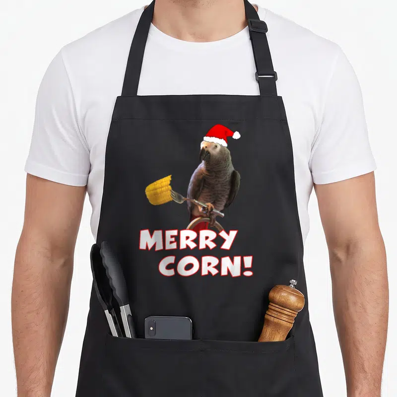 Merry african aprons - Grey parrot Santa hat fork corn MERRY CORN text — shown on a black cotton canvas apron against a white background