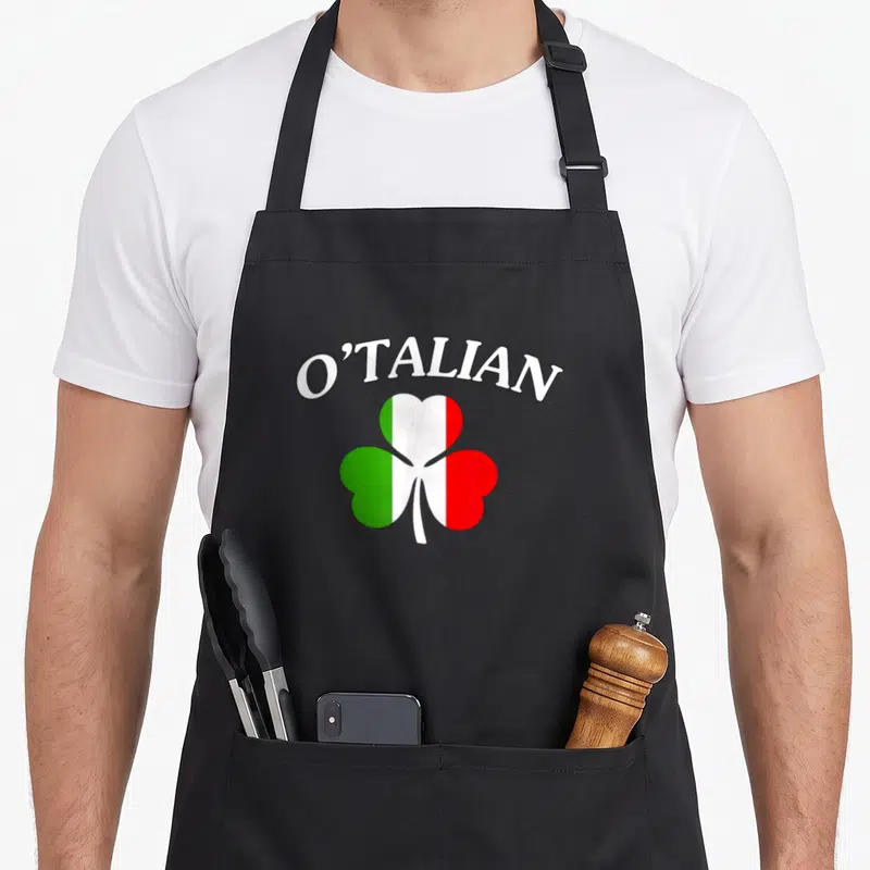 Otalian italy apron - Arched O'TALIAN text above a shamrock filled with green white and red Italian flag stripes — shown on a black cotton canvas apron against a white background