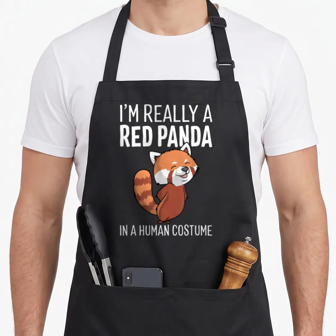 Panda human halloween apron - Red panda cartoon between I'M REALLY A RED PANDA IN A HUMAN COSTUME text — shown on a black cotton canvas apron against a white background
