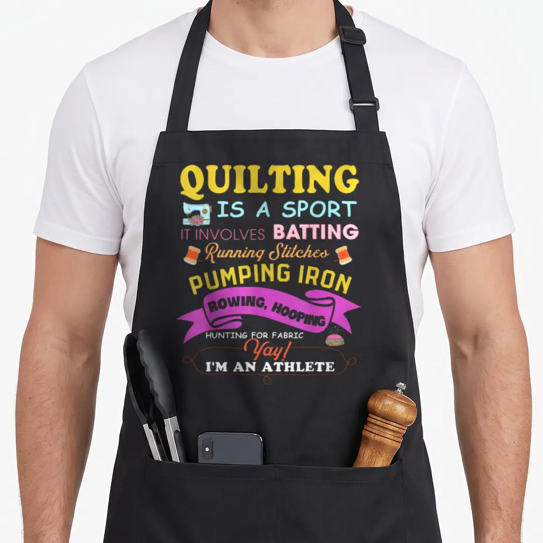 Sport quilt apron - Quilting Is A Sport text with sewing machine, thread spools, ribbon, and pincushion in yellow pink — shown on a black cotton canvas apron against a white background