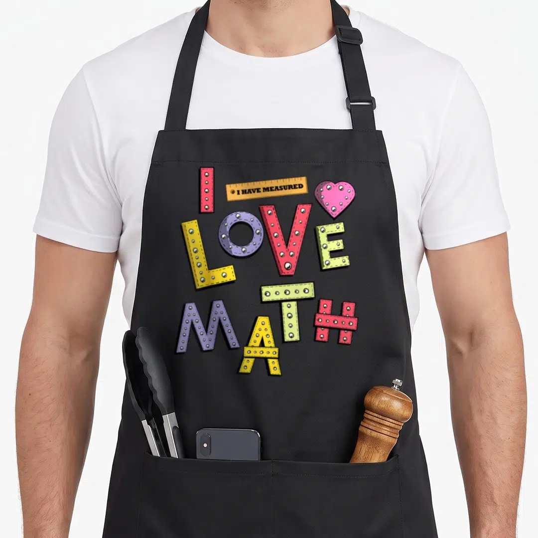 Mathematician teacher apron - I LOVE MATH studded letters with ruler reading I HAVE MEASURED and pink heart in red — shown on a black cotton canvas apron against a white background