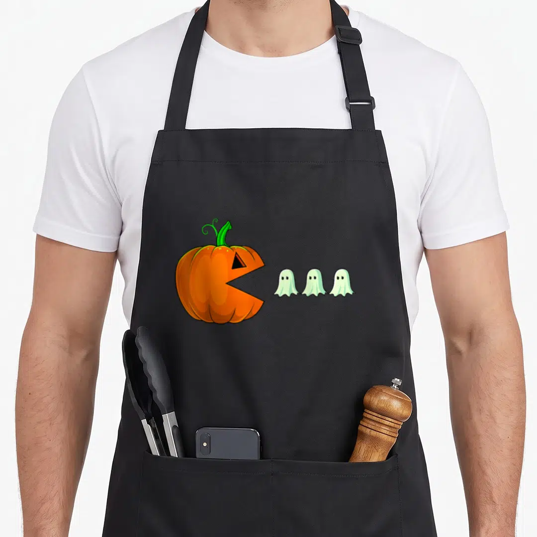 Pumpkin ghost halloween apron - Orange cartoon pumpkin with open mouth facing three small white ghosts in a row — shown on a black cotton canvas apron against a white background