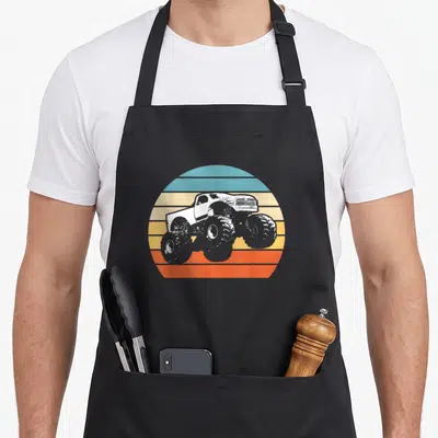 Racing truck aprons - White monster truck silhouette on retro blue yellow orange striped circle — shown on a black cotton canvas apron against a white background