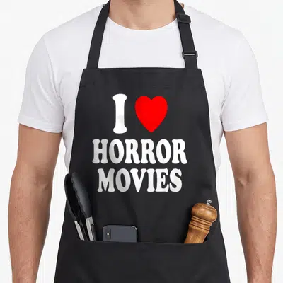 Scary horror apron - White I and red heart above stacked Horror Movies text — shown on a black cotton canvas apron against a white background
