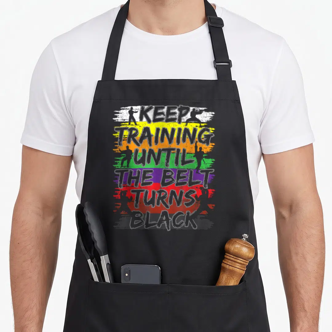 Belt training apron - Stacked text over colored brushstrokes with martial arts silhouettes — shown on a black cotton canvas apron against a white background