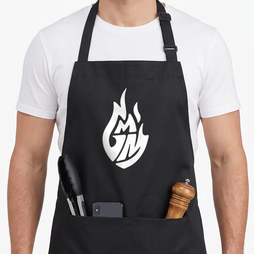 Vintage good mythical morning apron - White flame logo with integrated G and M letters in minimalist style — shown on a black cotton canvas apron against a white background