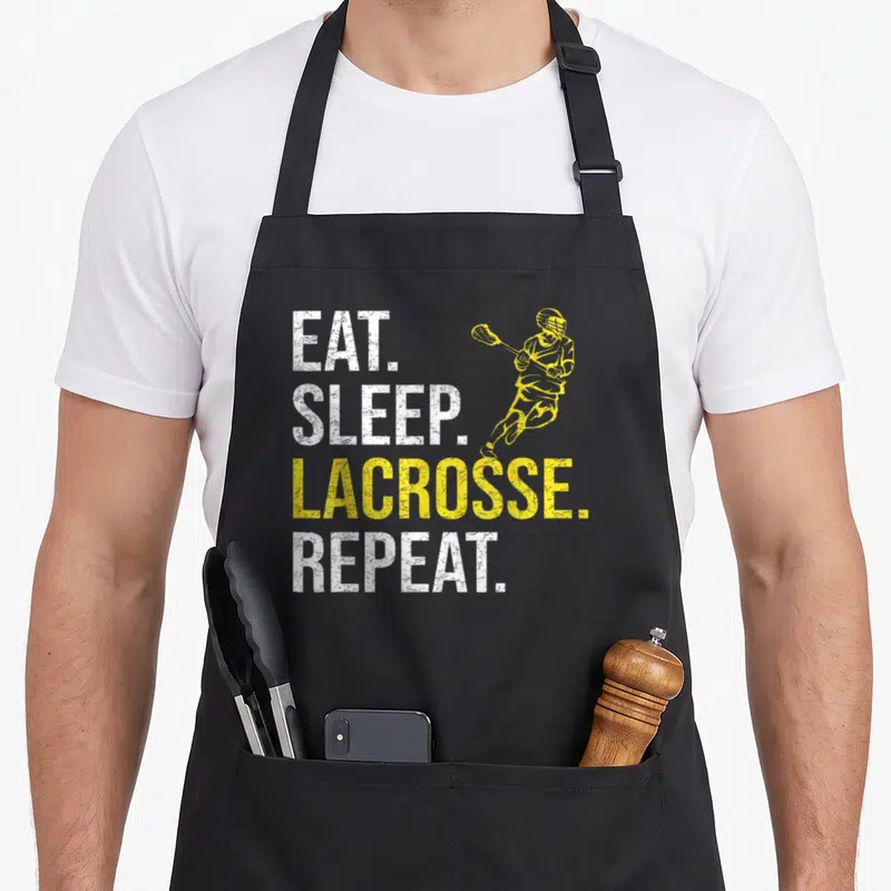 Eat father day apron - EAT SLEEP LACROSSE REPEAT text with running yellow player silhouette in distressed style — shown on a black cotton canvas apron against a white background
