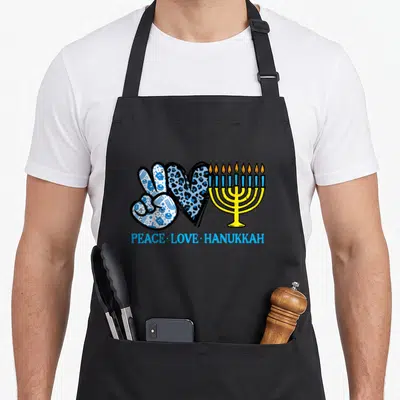 Peace chanukah hanukkah apron - Peace sign with dreidels, leopard heart, yellow menorah, and blue text — shown on a black cotton canvas apron against a white background