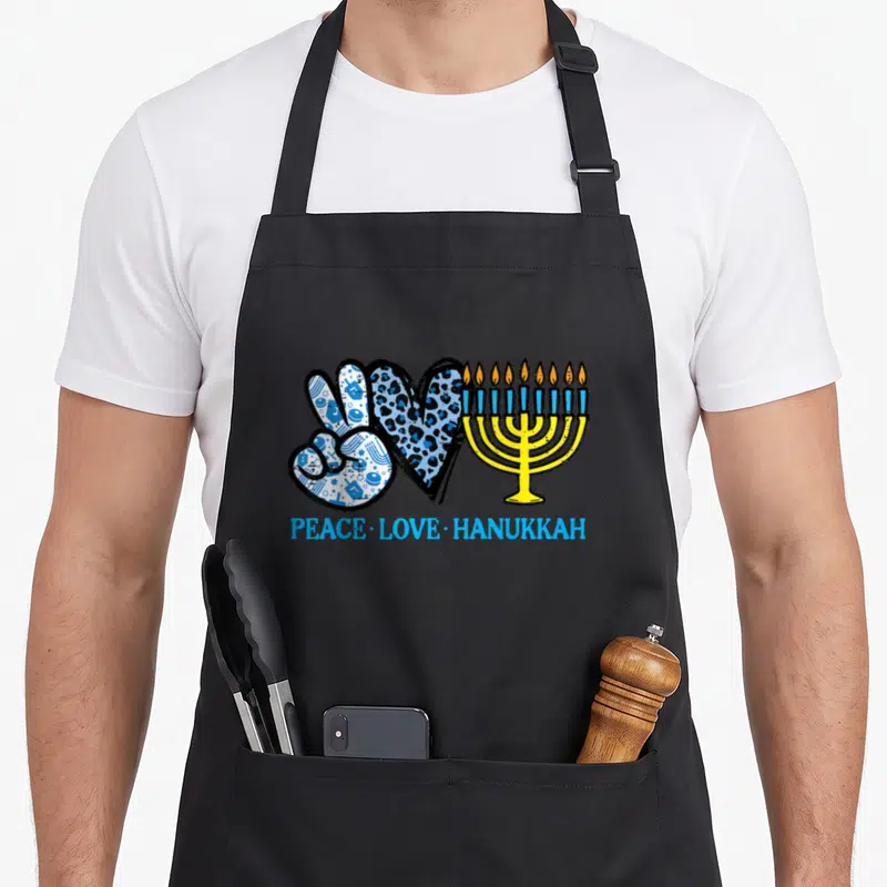 Peace chanukah hanukkah apron - Peace sign with dreidels, leopard heart, yellow menorah, and blue text — shown on a black cotton canvas apron against a white background