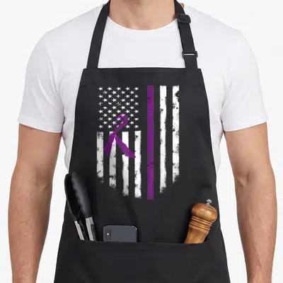 Cystic american flag apron - Distressed white flag with purple vertical stripe and awareness ribbon overlaying stars — shown on a black cotton canvas apron against a white background
