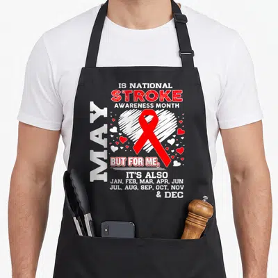 May i love production apron - Red stroke awareness ribbon over white heart with monthly text listing January through — shown on a black cotton canvas apron against a white background