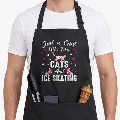 Ice cat apron - Stacked white text reading Just a Girl Who Loves CATS And ICE SKATING with multicolored cat and pink — shown on a black cotton canvas apron against a white background