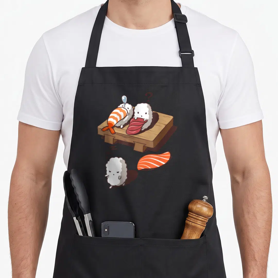 Sleep sushi apron - Cartoon sushi with detached salmon, wooden board, and zzz sleep symbols — shown on a black cotton canvas apron against a white background