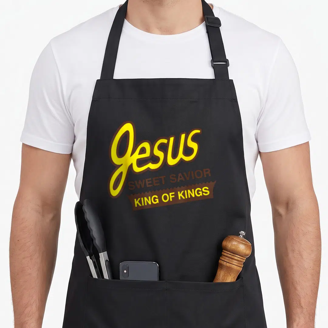 Jesus king of the grill apron - Yellow and brown typography reading Jesus Sweet Savior King of Kings inside a banner — shown on a black cotton canvas apron against a white background