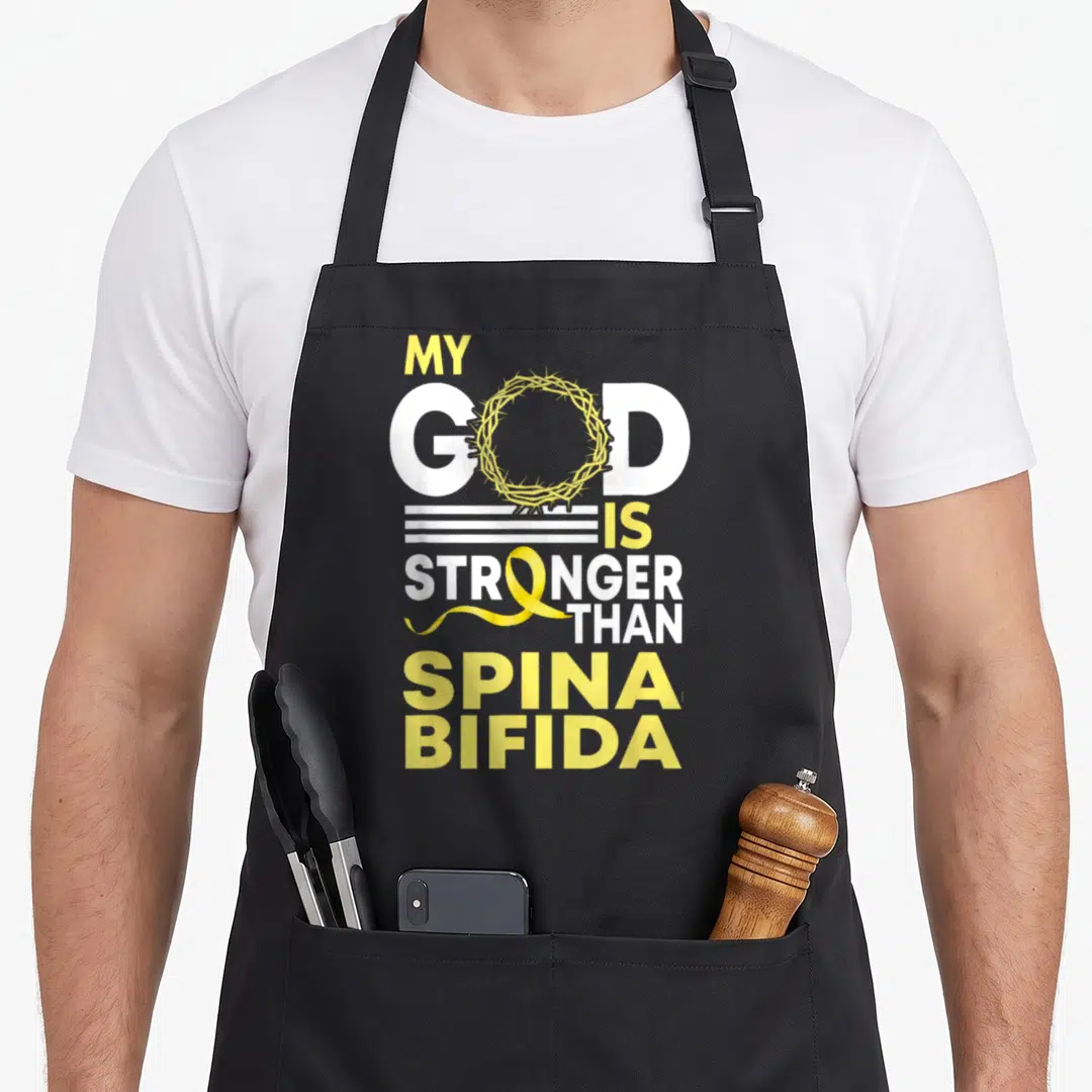 Spina ribbon apron - Yellow awareness ribbon and crown of thorns overlaying MY GOD IS STRONGER THAN SPINA BIFIDA text — shown on a black cotton canvas apron against a white background