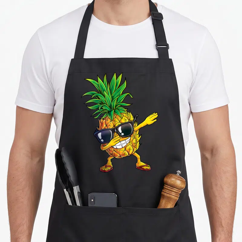 Dabbing pineapple apron - Cartoon pineapple wearing black sunglasses and red flip-flops in a dab pose — shown on a black cotton canvas apron against a white background