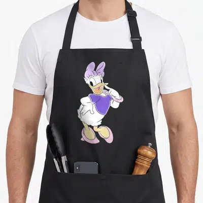 Unicorn daisy apron - Centered cartoon duck in purple top and pink shoes on white body — shown on a black cotton canvas apron against a white background