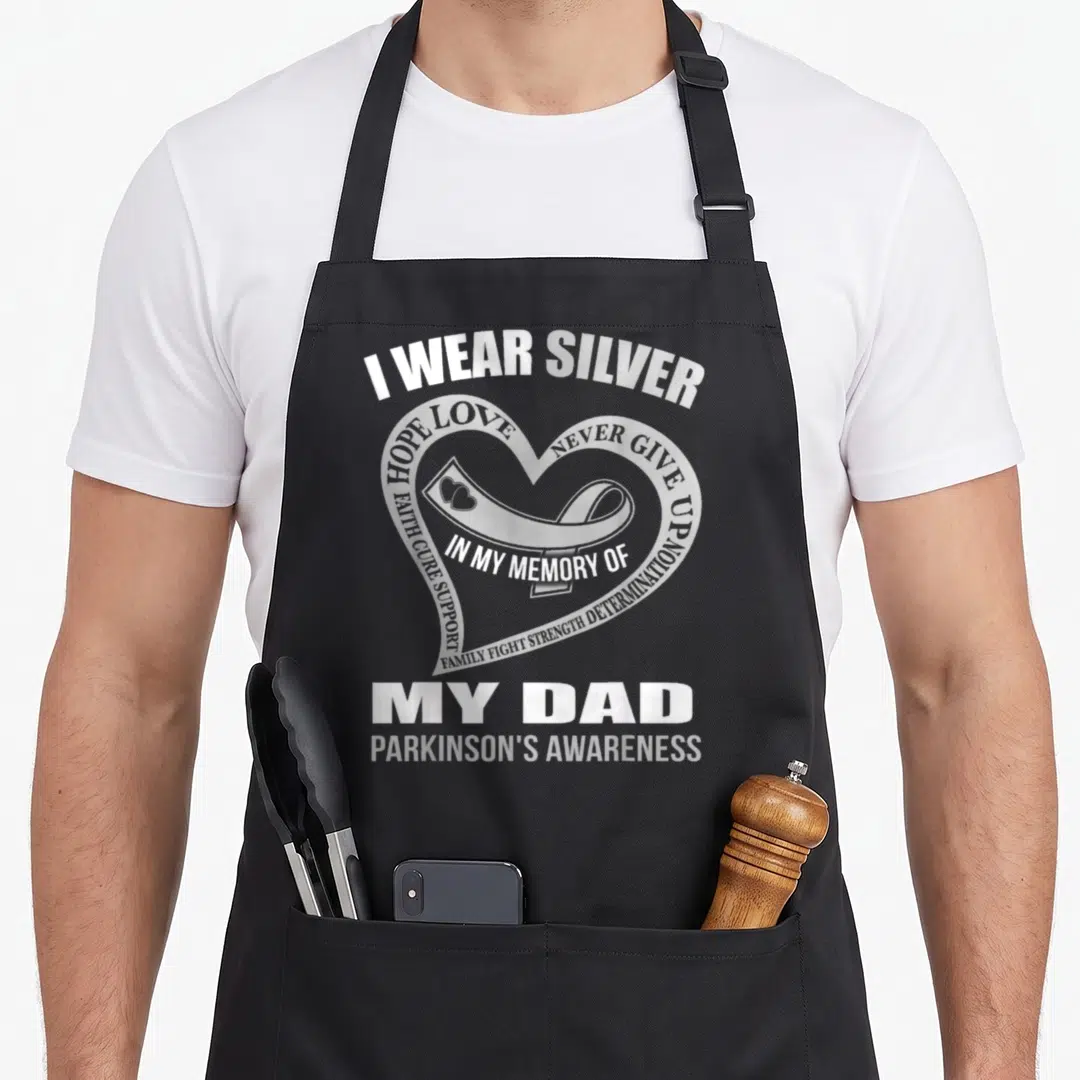 Parkinson memory apron - Silver ribbon inside heart with white text I WEAR SILVER MY DAD PARKINSONS AWARENESS — shown on a black cotton canvas apron against a white background