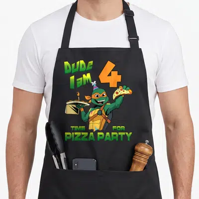 Mikey pizza apron - Cartoon turtle holding pizza box and slice with green and orange text celebrating age four — shown on a black cotton canvas apron against a white background