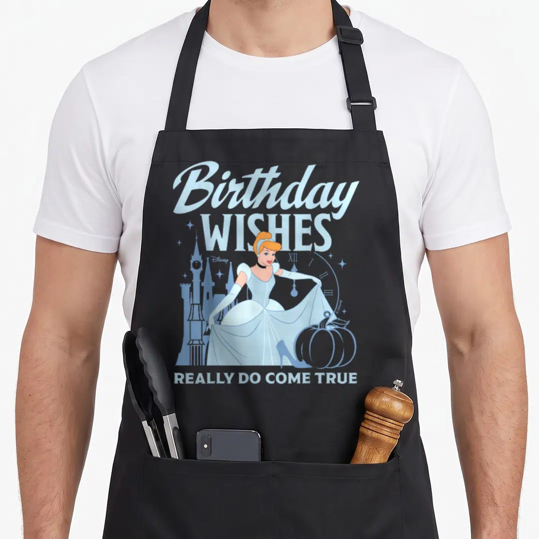 Birthday cinderella apron - Cinderella in blue dress with pumpkin and castle under Birthday Wishes Really Do Come True — shown on a black cotton canvas apron against a white background