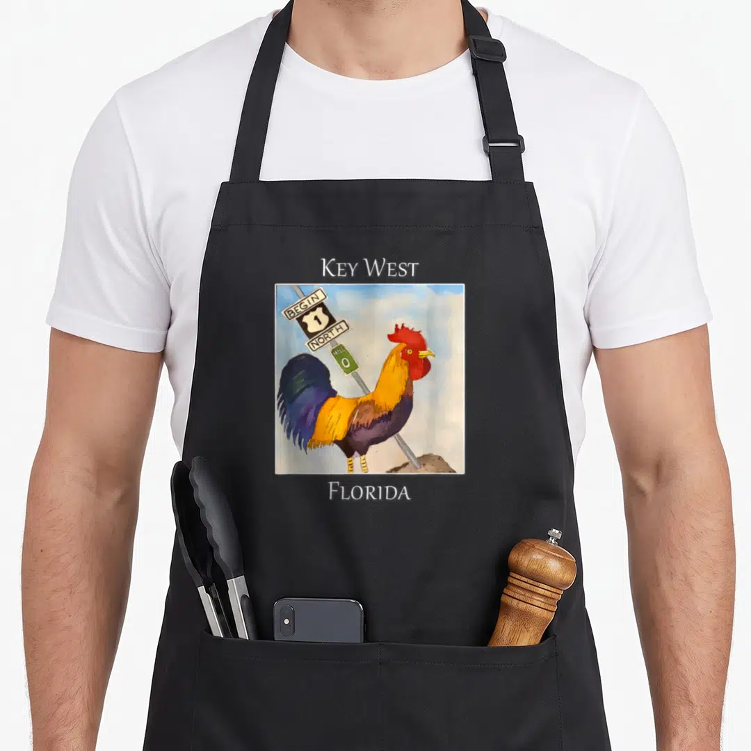 Mile rooster apron - Watercolor rooster beside Key West Begin North 1 Mile 0 Florida sign — shown on a black cotton canvas apron against a white background