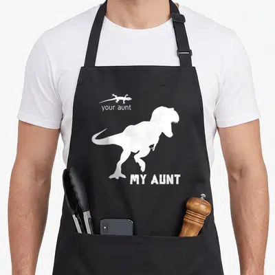 Squad best aunt ever apron - White T-Rex and lizard silhouettes with your aunt MY AUNT text on black — shown on a black cotton canvas apron against a white background