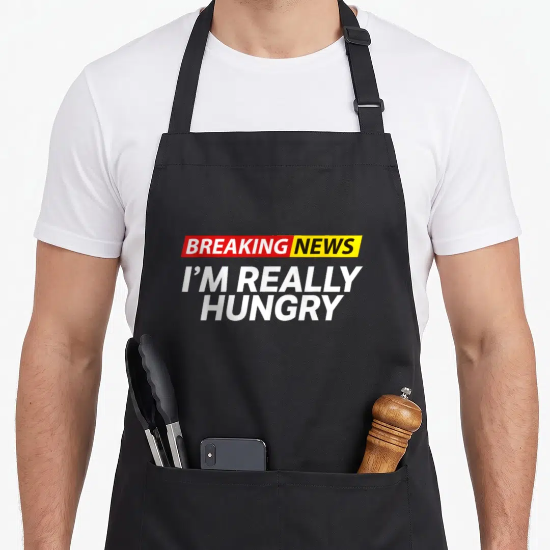 Breaking food aprons - Red yellow and white stacked text reading Breaking News I'm Really Hungry — shown on a black cotton canvas apron against a white background