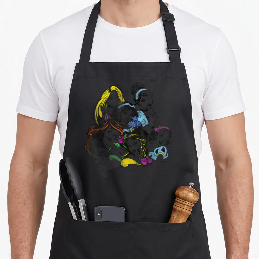 Bold princess apron - Six cartoon princess faces in yellow blue pink purple with flowers at bottom — shown on a black cotton canvas apron against a white background