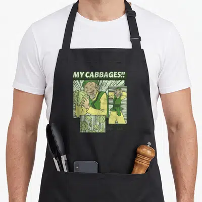 Merchant cabbage apron - Cabbage Man comic panels with MY CABBAGES!! text and AVATAR logo in green yellow beige — shown on a black cotton canvas apron against a white background