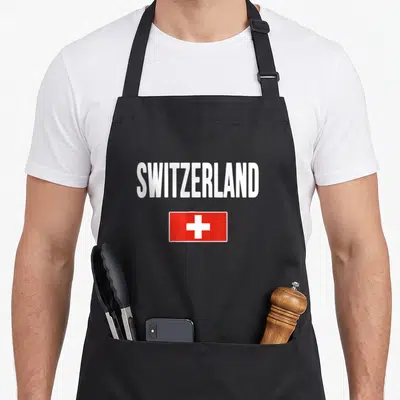 Switzerland swiss apron - SWITZERLAND text above red flag with white cross — shown on a black cotton canvas apron against a white background