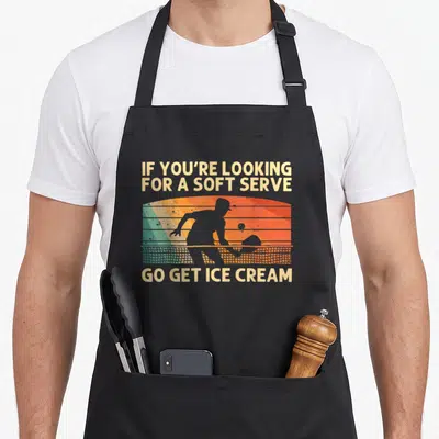 Player pickle apron - Retro tennis player silhouette against orange sunset with text IF YOU'RE LOOKING FOR A SOFT SERVE — shown on a black cotton canvas apron against a white background