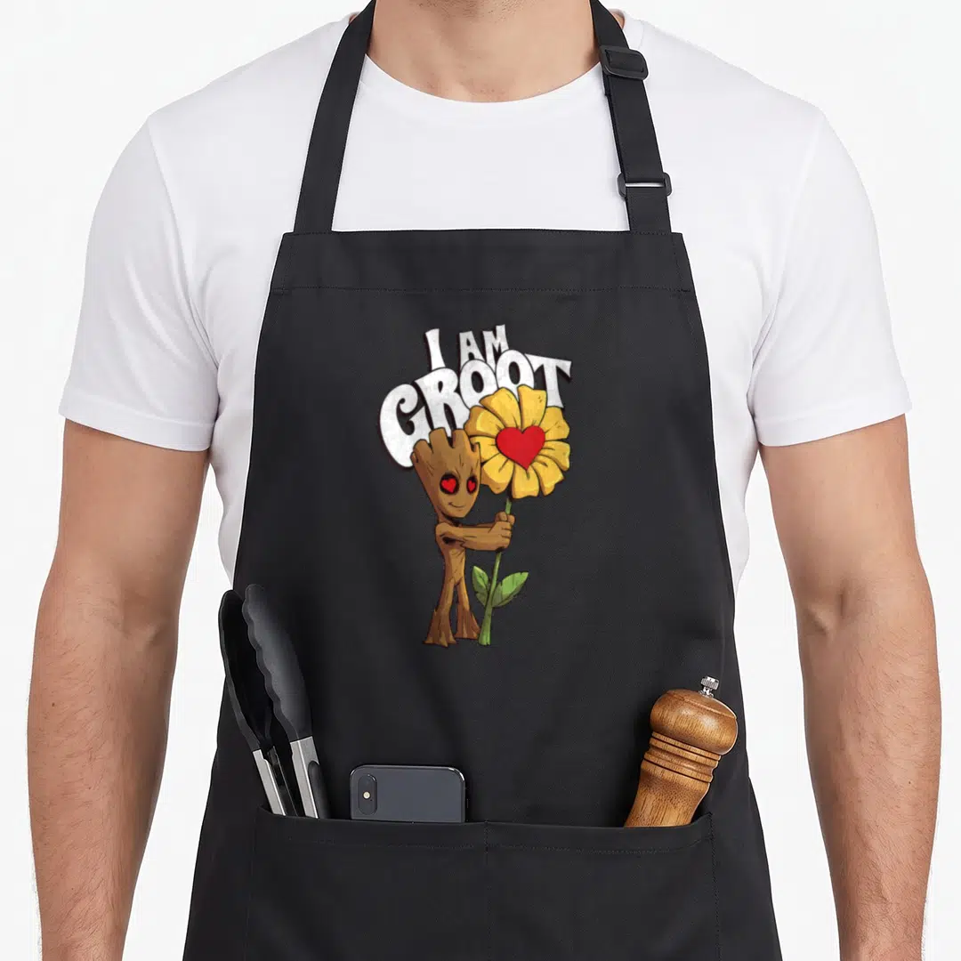 Eye sunflower apron - I AM GROOT text above cartoon character holding yellow sunflower with red heart center — shown on a black cotton canvas apron against a white background