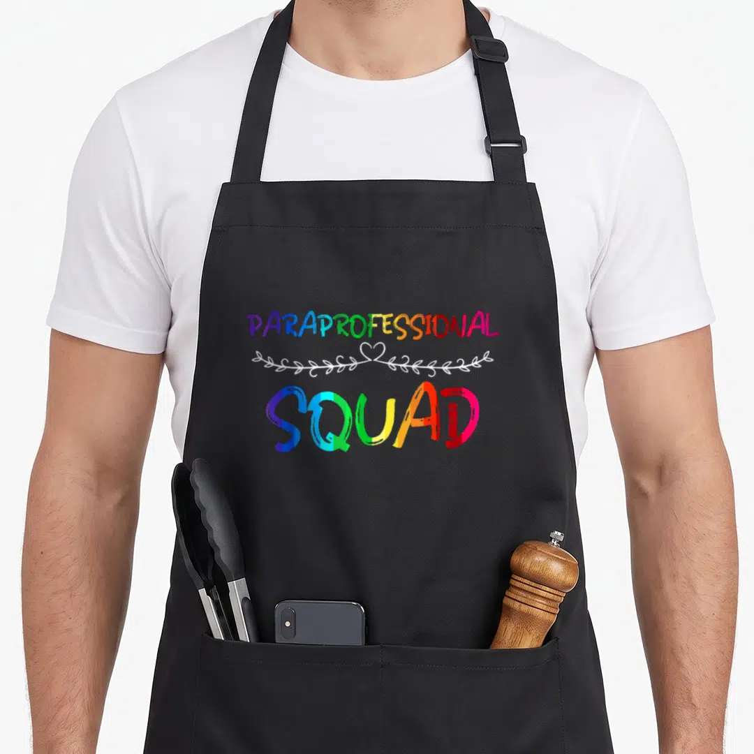 Paraprofessional squad teacher apron - Rainbow text PARAPROFESSIONAL SQUAD with white vine and heart separator — shown on a black cotton canvas apron against a white background