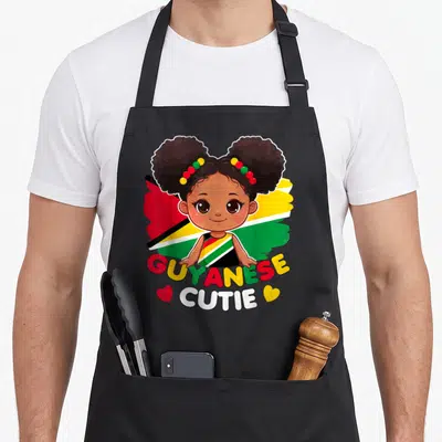 Guyanese princess apron - Cartoon girl with afro puffs in front of red yellow green flag with GUYANESE CUTIE text — shown on a black cotton canvas apron against a white background