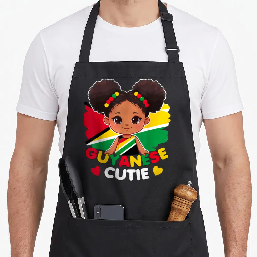 Guyanese princess apron - Cartoon girl with afro puffs in front of red yellow green flag with GUYANESE CUTIE text — shown on a black cotton canvas apron against a white background