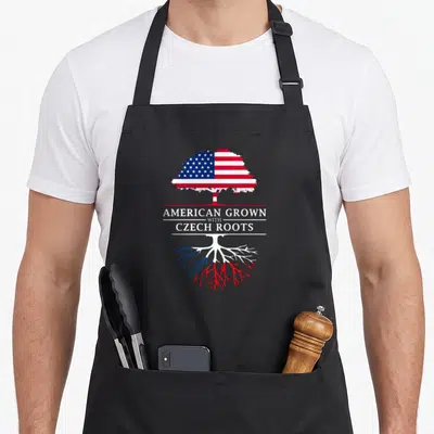 Grown czech apron - Tree with US flag canopy and red blue roots displaying American Grown with Czech Roots text — shown on a black cotton canvas apron against a white background