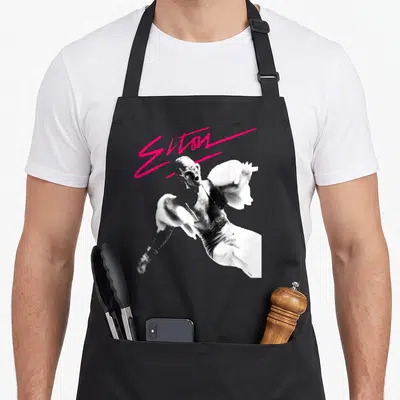 Elton birthday pink apron - Pink script reading Elton above black and white photo of man singing — shown on a black cotton canvas apron against a white background