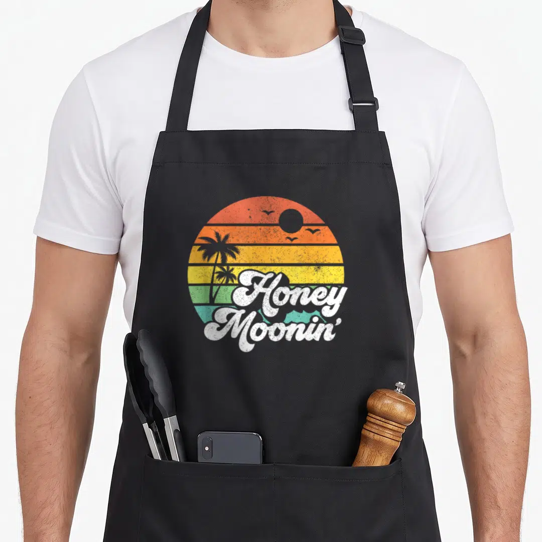 Honey couple apron - Retro circular sunset with striped red orange yellow green teal background and white Honey Moonin — shown on a black cotton canvas apron against a white background