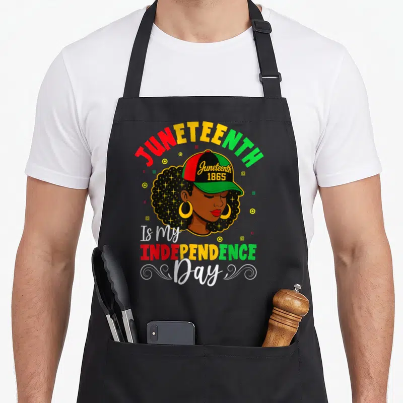 Cute juneteenth independence apron - Cartoon woman wearing a cap with JUNETEENTH 1865 and Is my INDEPENDENCE Day text — shown on a black cotton canvas apron against a white background