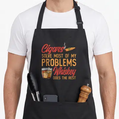Solve bourbon apron - Cigars Solve Most Of My Problems Whiskey Does The Rest with cigar and whiskey glass in red — shown on a black cotton canvas apron against a white background