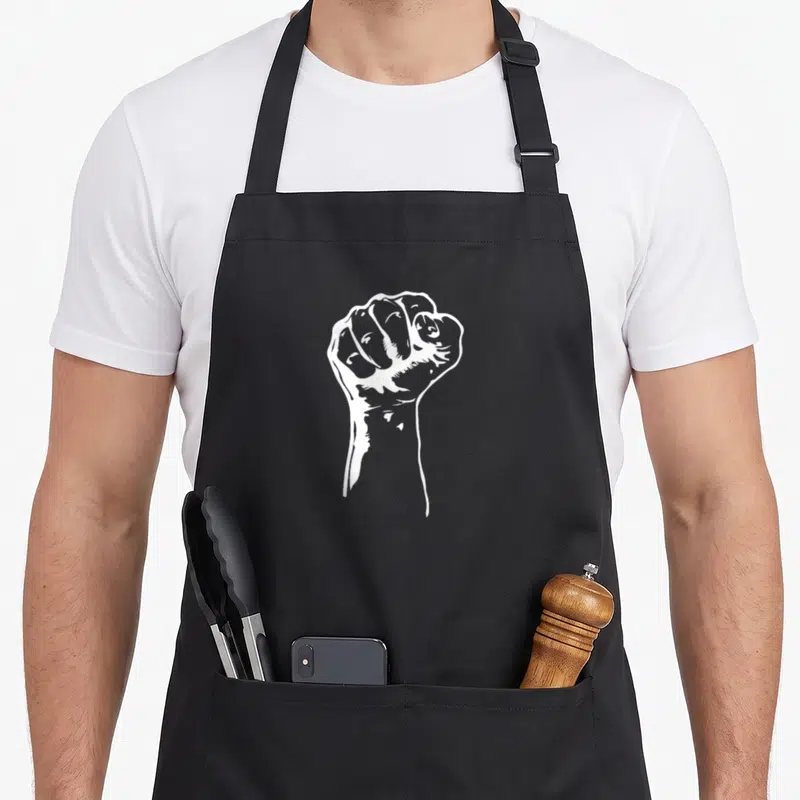 Right blm camping apron - White line-art illustration of a clenched fist centered on a dark background — shown on a black cotton canvas apron against a white background