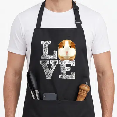 Guinea crazy pig lady apron - Realistic guinea pig in white brown tan replacing O in LOVE text — shown on a black cotton canvas apron against a white background