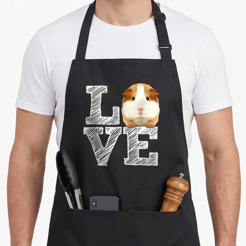 Guinea crazy pig lady apron - Realistic guinea pig in white brown tan replacing O in LOVE text — shown on a black cotton canvas apron against a white background