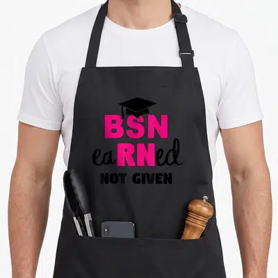 Earned nursing aprons - BSN earned not given text with black graduation cap in pink and black typography — shown on a black cotton canvas apron against a white background