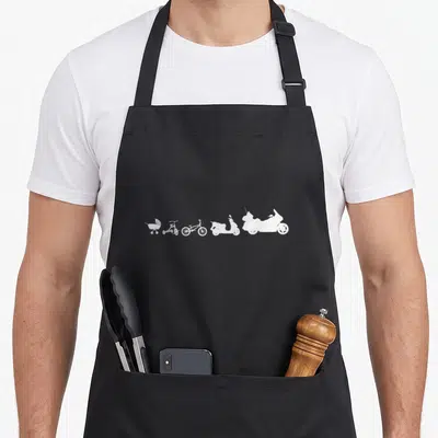 Evolution biker apron - Five white silhouettes in a row: stroller, tricycle, bicycle, scooter, motorcycle — shown on a black cotton canvas apron against a white background