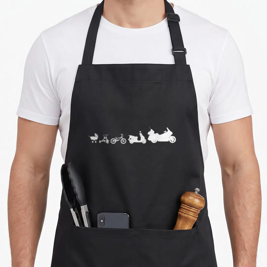 Evolution biker apron - Five white silhouettes in a row: stroller, tricycle, bicycle, scooter, motorcycle — shown on a black cotton canvas apron against a white background