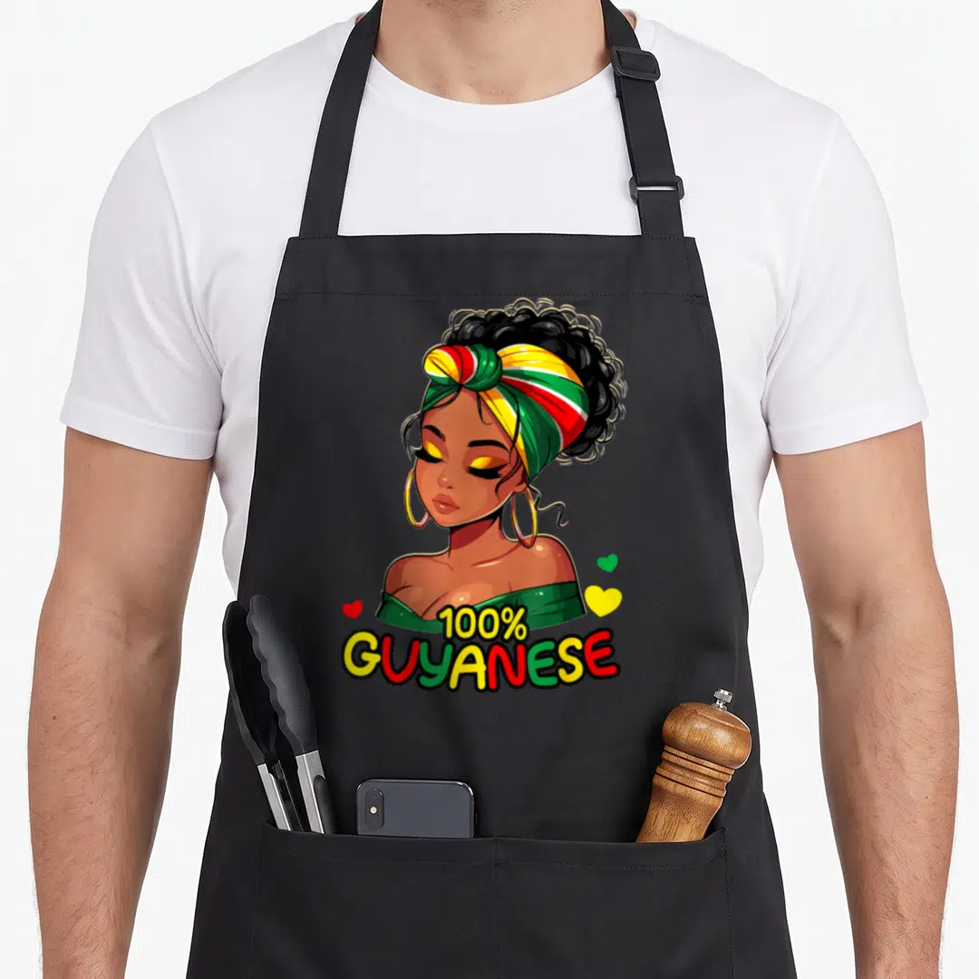 Guyanese messy aprons - Cartoon woman with striped headwrap, 100% GUYANESE text, three hearts — shown on a black cotton canvas apron against a white background